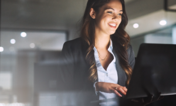 Woman smiling and working on a laptop in a professional environment.