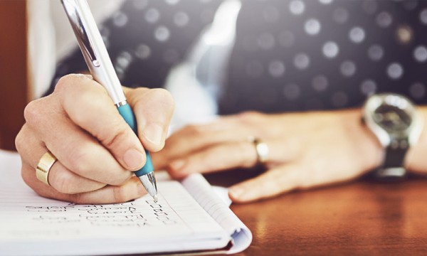 Hands writing on a notepad with a checklist, with a watch on the wrist in the background.
