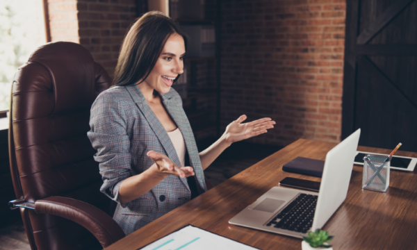 Woman in business suit sitting in an office chair at her desk with a laptop and paperwork.