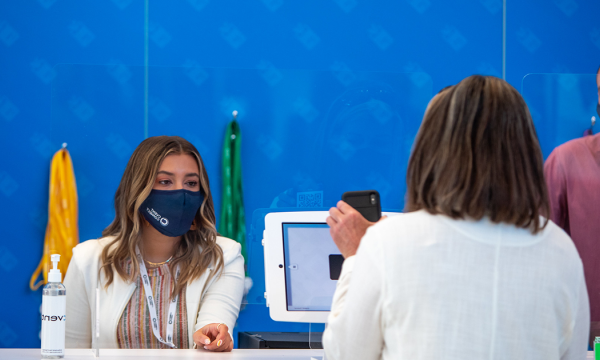 A person with mask is checking in at a desk with sanitizer and a monitor for health check.