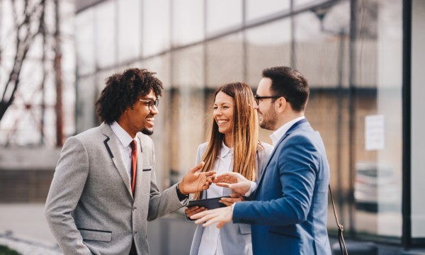 Two men and a woman in business attire network outside a commercial property.