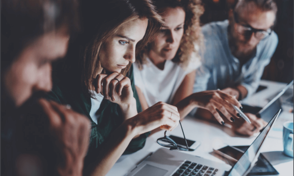 Group of people sitting around a laptop, working together and collaborating on a project.