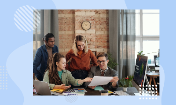 A group of people in an office with a brick wall, a clock, and a computer.
