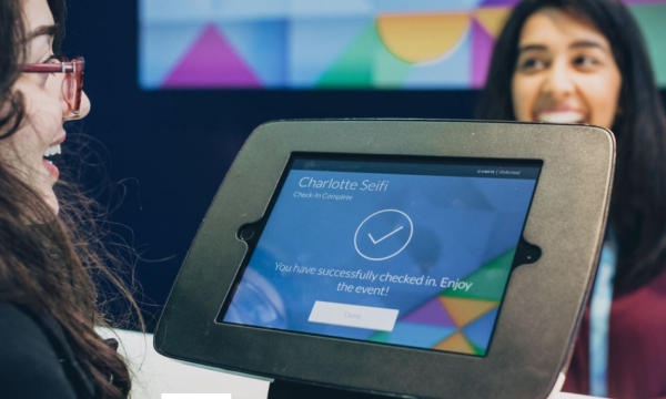 Charlotte Seif is checked in, and a happy woman is standing behind a machine with a colorful background.