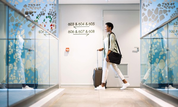 A bleisure traveler at a hotel, walking with luggage, with modern decor and natural light.