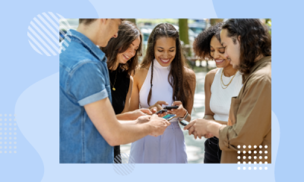 Group of five people standing close together looking at their phones on a bright, sunny day.