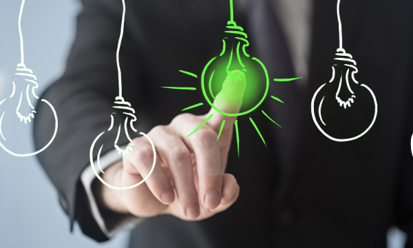A businessman touches a green light bulb with three light bulbs hanging from the ceiling in the background.