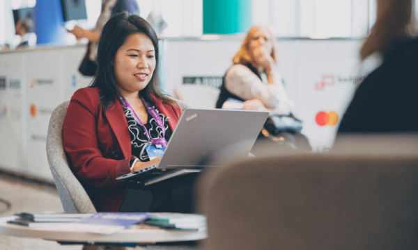 A woman is sitting on a chair and working on her laptop at the CVENT booth.