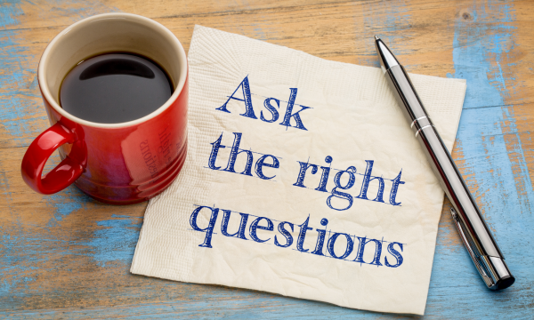 A cup of coffee, pen, and napkin with "Ask the right questions" written on it.