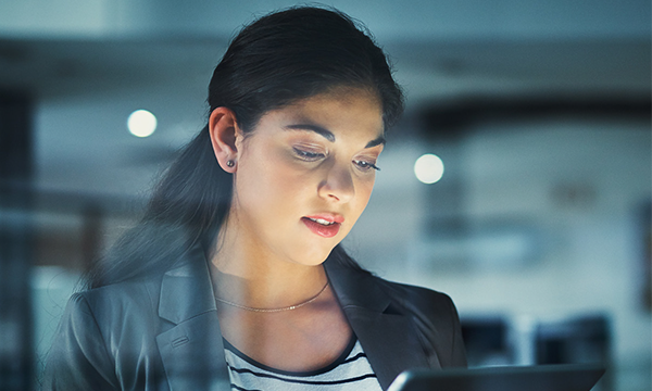 A woman with black hair is holding a tablet while standing in front of a blurred background.