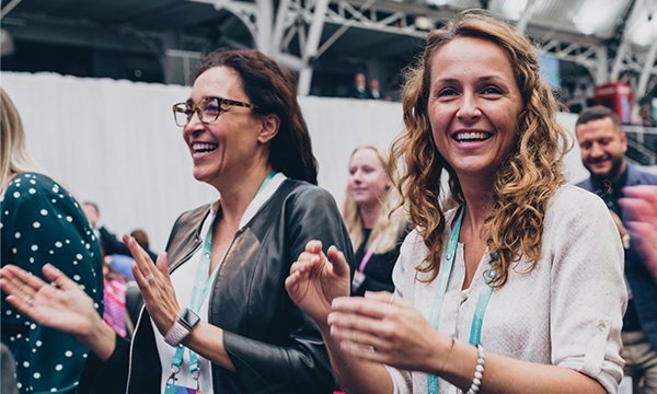 Two women wearing green lanyards clapping their hands and smiling at a conference.