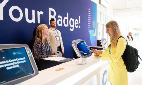 Two women are at a counter with a sign that says "Your Badge!" at a Cvent event.