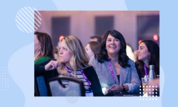 Women laughing with each other at a conference with others in the background.