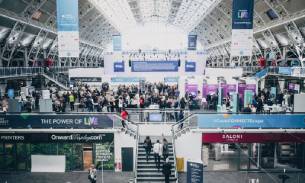 People walking around in a crowded conference space with lots of banners, signs, and architectural structures.