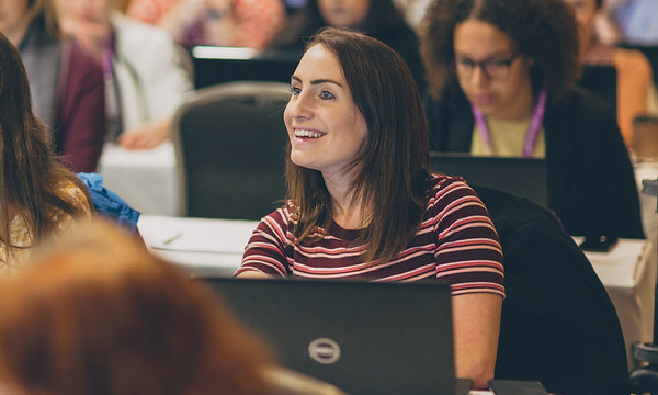 A woman sitting in front of a laptop computer at an online demo at a conference.