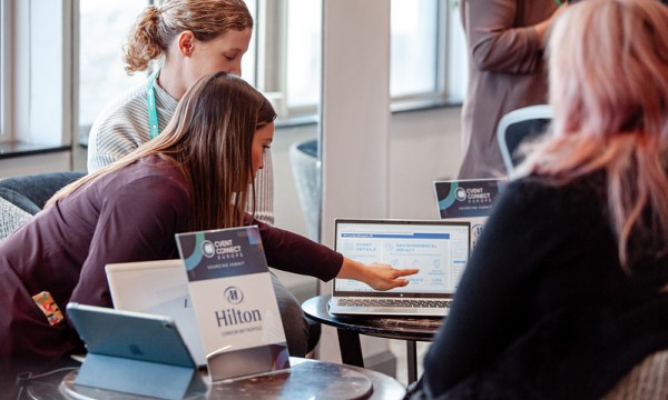 Three women at a conference, using a laptop, with Hilton and Cvent Connect branding present in the image.