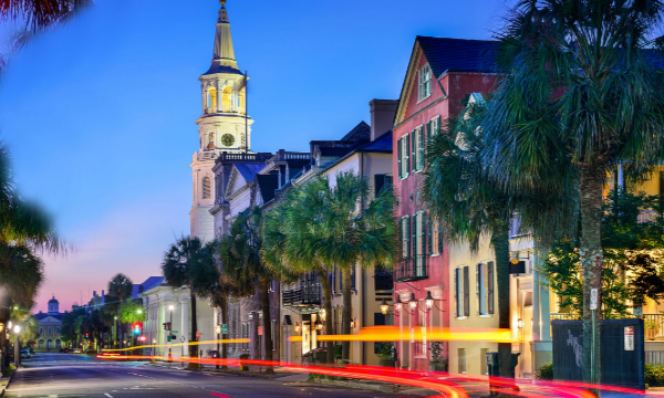 A blurred street with a church and trees in Charleston, SC, at dusk.