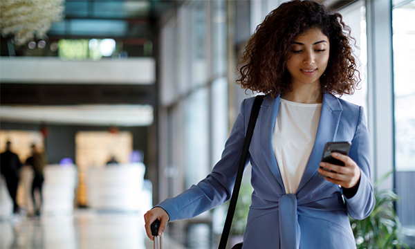 A woman with luggage in an airport checks her phone while waiting for her flight.