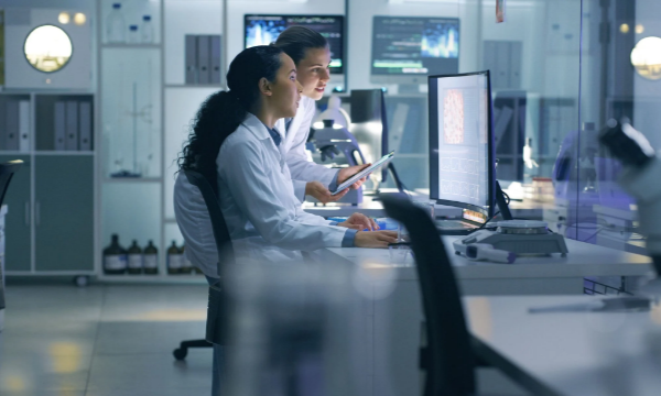 Two scientists in lab coats looking at a computer monitor in a laboratory setting.