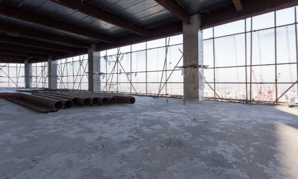 Concrete floor, glass walls, and steel bars in an unfinished room of a building under construction.