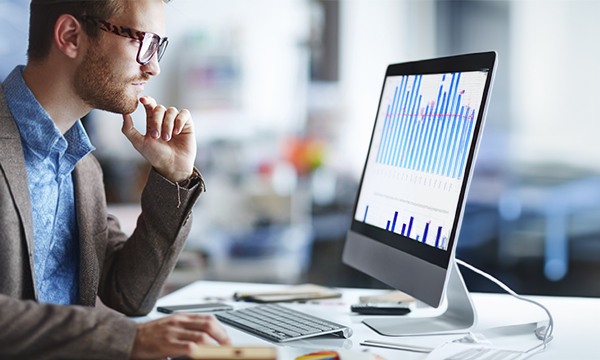 Businessman looking at computer screen with graph chart on it, pondering how to skyrocket revenue.
