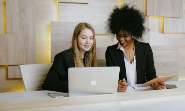 Two women working at a desk with a laptop and notepad in an office at Propertybase.