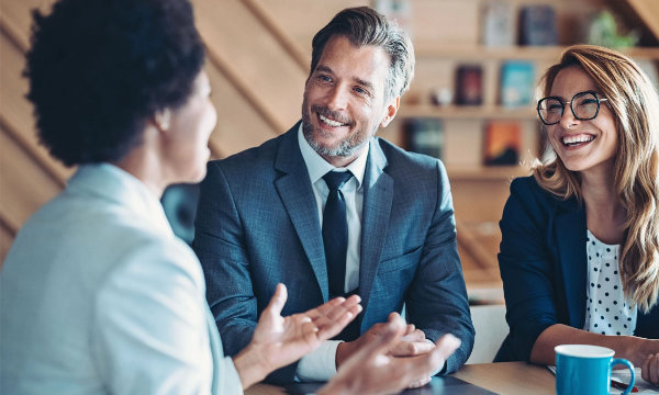 A man and two women are sitting at a table, smiling and looking at each other.
