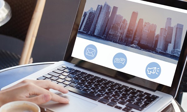 A laptop with a cityscape on the screen and a hand typing on the keyboard.