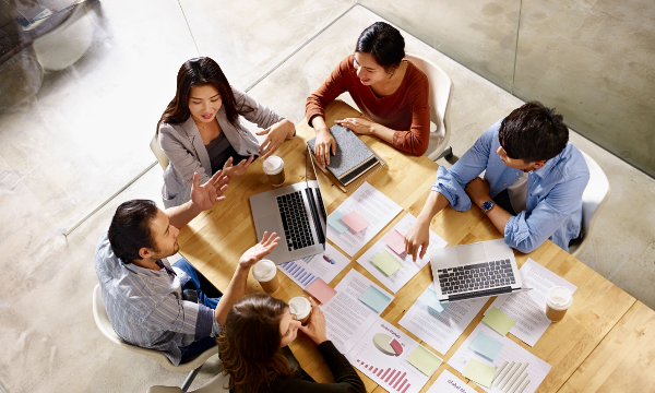 Group of people having a meeting around a table with laptops and graphs on it.