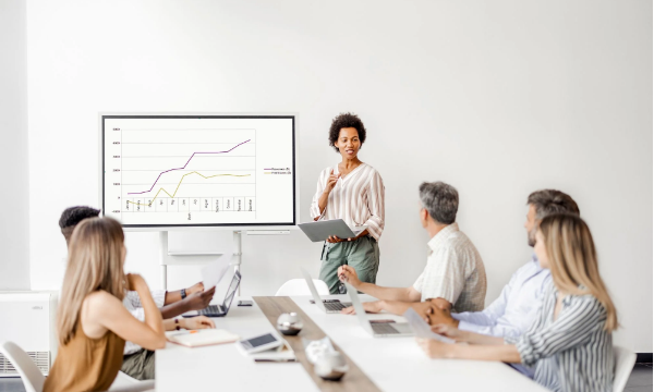 A group of people are sitting in front of a woman giving a presentation.