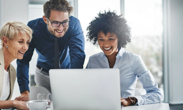 Three people standing and looking at a laptop with a smile on their faces in an office.