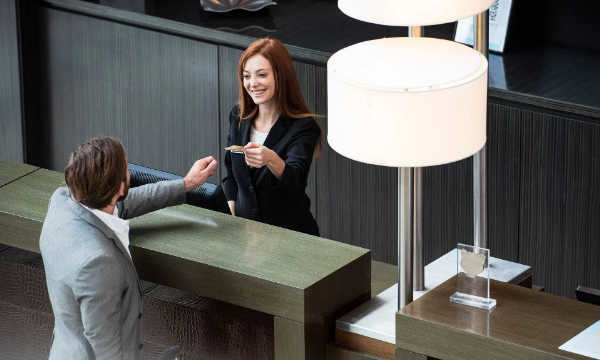 A guest receives a key card from a smiling hotel receptionist at the front desk.