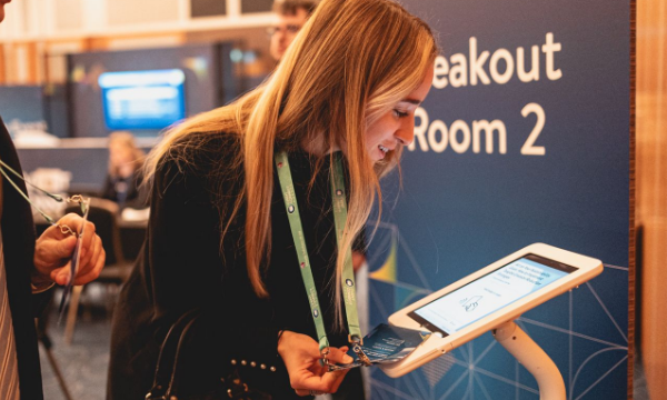Woman looking at a tablet that is standing on a stand in front of a breakout room sign.