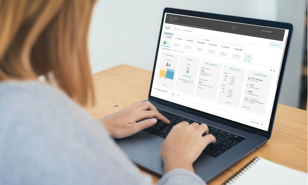 A woman works on a laptop with graphs and charts displayed on the screen.