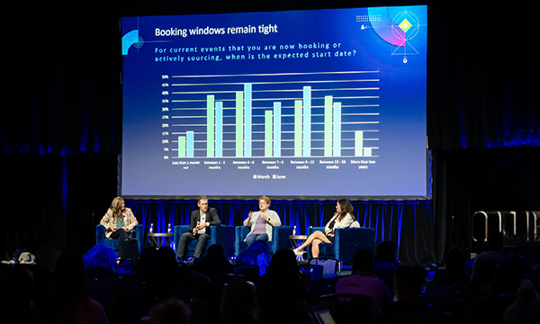 A panel of experts discuss financial events on stage in front of an audience.