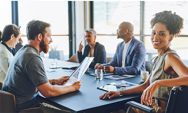 A group of people sitting around a conference table with papers and cups on top of it.