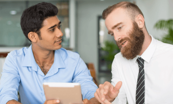 Two men in an office setting, one holding a tablet, engaging in a conversation.