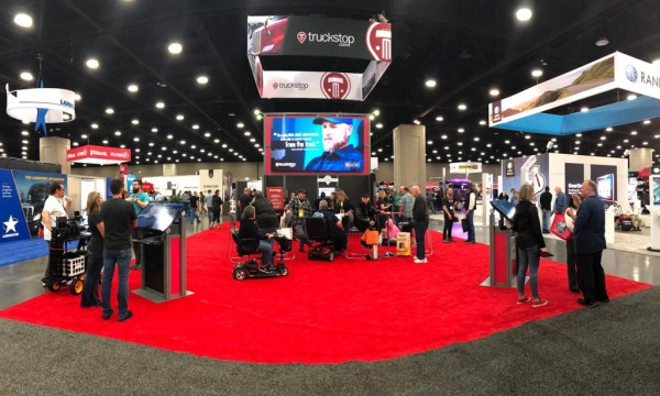 People are gathered at a trade show with a Truckstop banner hanging from the ceiling.