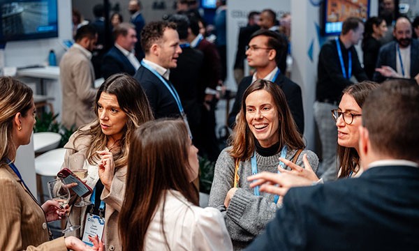 Several people are gathered at a conference, with one woman holding a glass of wine and speaking to others.