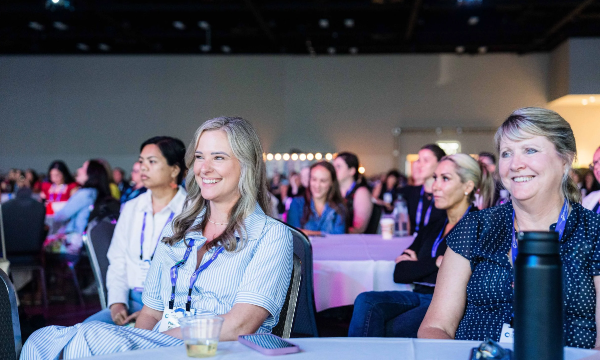Three women in a large conference room, with tables and chairs arranged for an event.