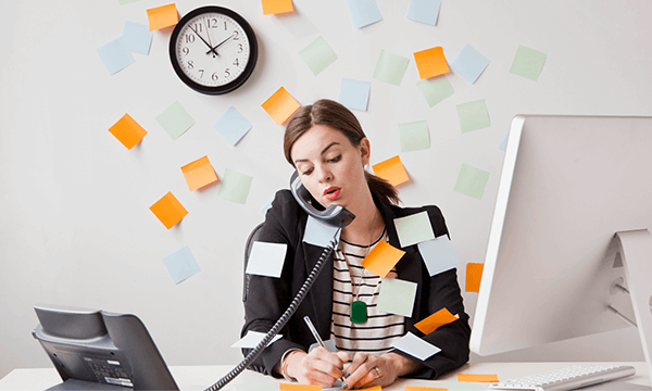 A woman with many sticky notes around her is working on a computer in an office.