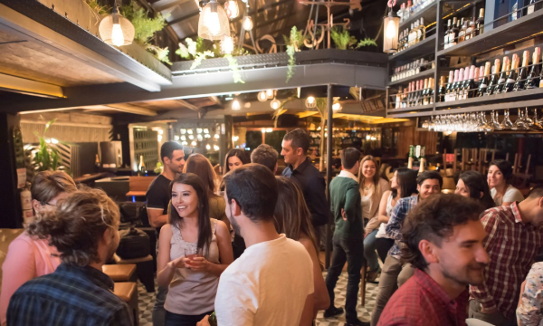Group of people standing and talking in a bar with shelves full of bottles on the walls.