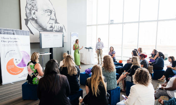 A group of people are attending a seminar in a room with glass walls and a portrait on the wall.