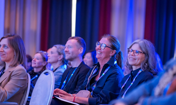 A group of smiling attendees in an event with blue curtains and a spotlight on the ceiling.
