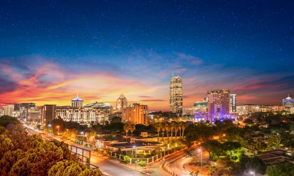 Nighttime cityscape of Sandton, South Africa, with modern architecture, trees, and a starlit sky.