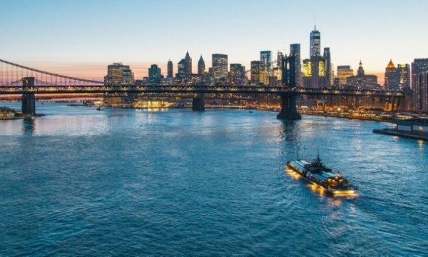 A bridge over a water body with a boat sailing and a city skyline in the background.