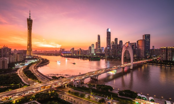 Guangzhou, China cityscape showing modern architecture and a bridge over the Pearl River at sunset.
