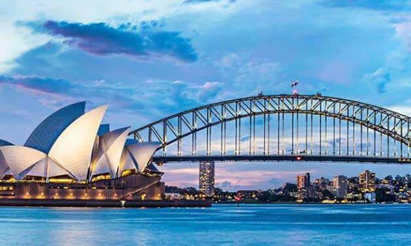 Sydney Opera House and Harbour Bridge with a city skyline at dusk, reflecting in blue waters.