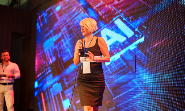 A woman is standing on stage at an event, holding a microphone and wearing a name tag.