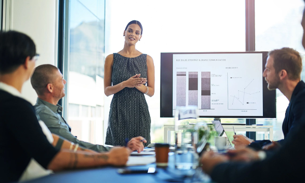 A woman is giving a presentation in front of a group of people in a meeting room.